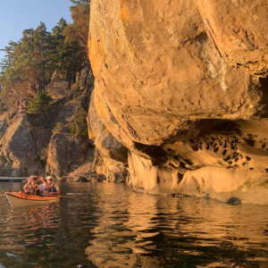 Kayakers paddling past golden sandstone cliffs on the Saturna Island sunset kayak tour