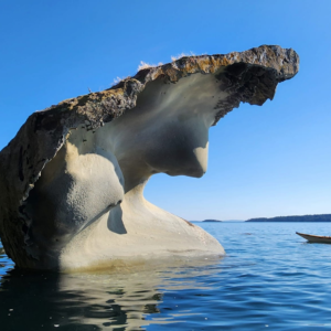 Kayaker paddling past a dramatic tafoni rock formation rising from the water along Saturna Island's south shore